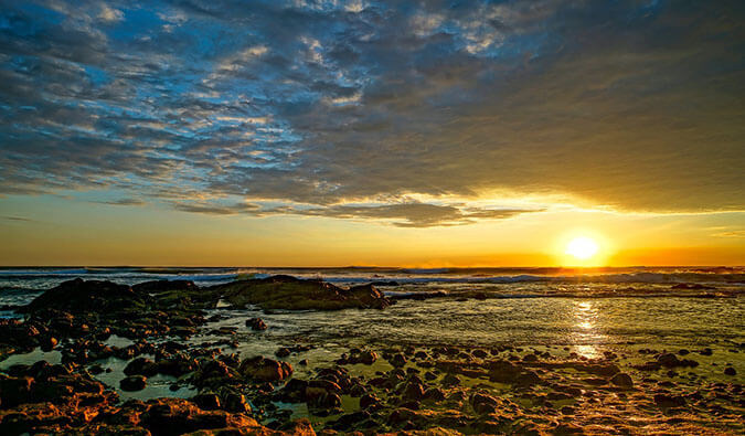 the sun setting over a rocky beach with the sun reflecting in the sea