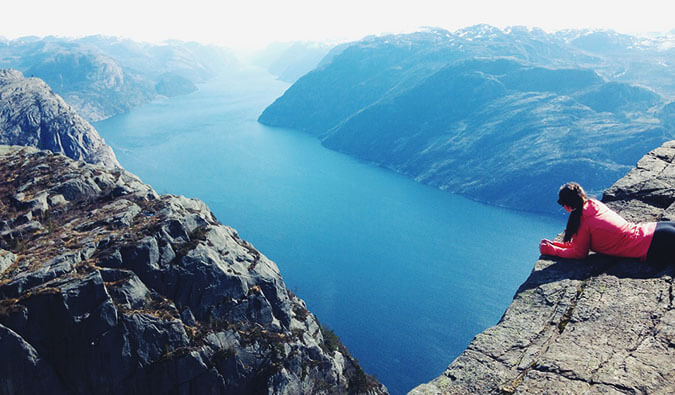 woman laying down on her front looking down from a cliff to a lake