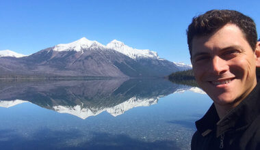 Nomadic Matt smiling towards the camera with mountains in the background reflecting in the water