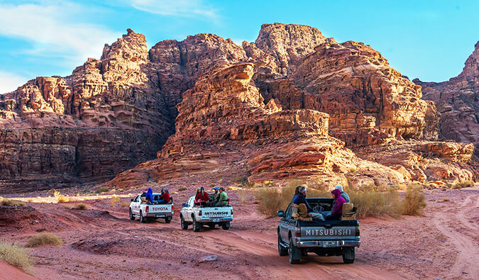 three trucks with people sat in the back traveling through Jordan