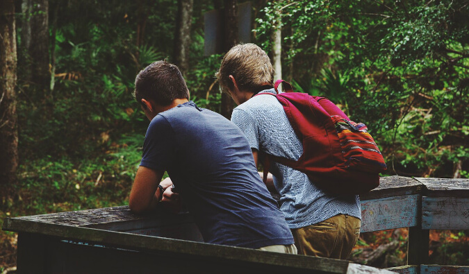 to men stood next to each other on a wooden bridge looking out into a forest