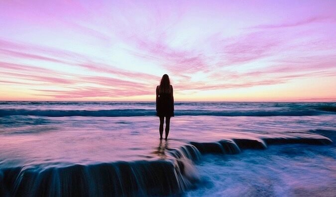 A woman looking out over the ocean at a pink sunset
