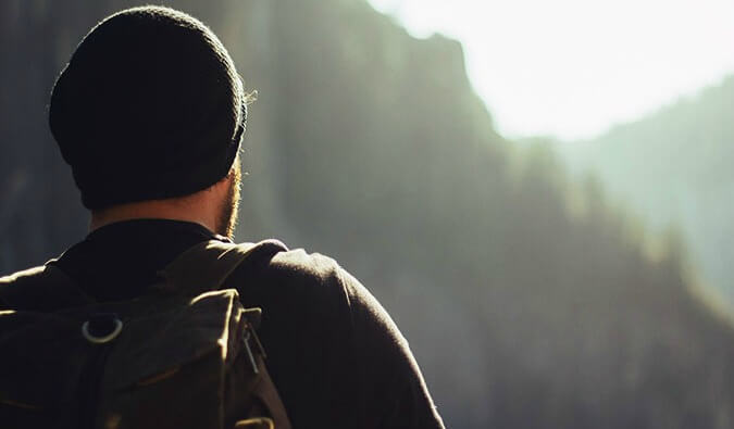 the back of a man wearing a hat and backpack looking out to the distance
