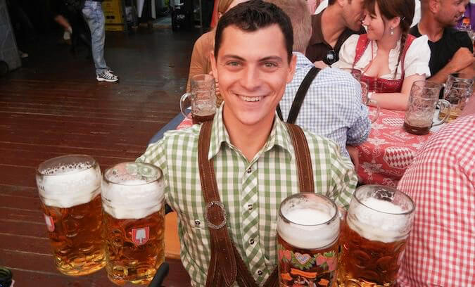 Nomadic Matt at Octoberfest wearing traditional clothes holding 4 pints of beer