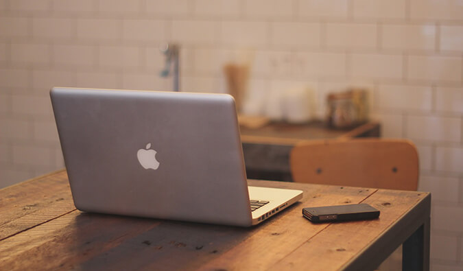 mac book pro open on a wooden table next to a mobile phone