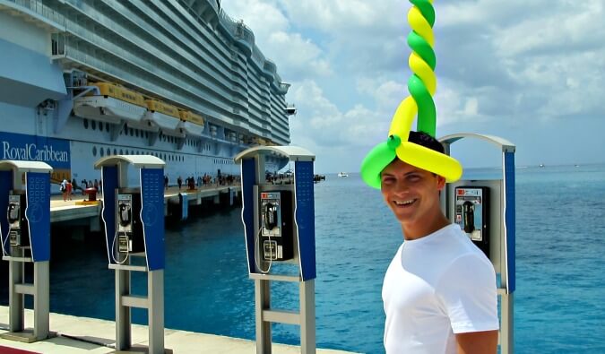 Nomadic Matt pictured with a balloon hat on at a port with a Royal Caribbean cruise ship in the background to the left