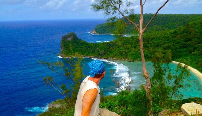 man sat front and centre looking down and out over the sea to the left and greenery to the right