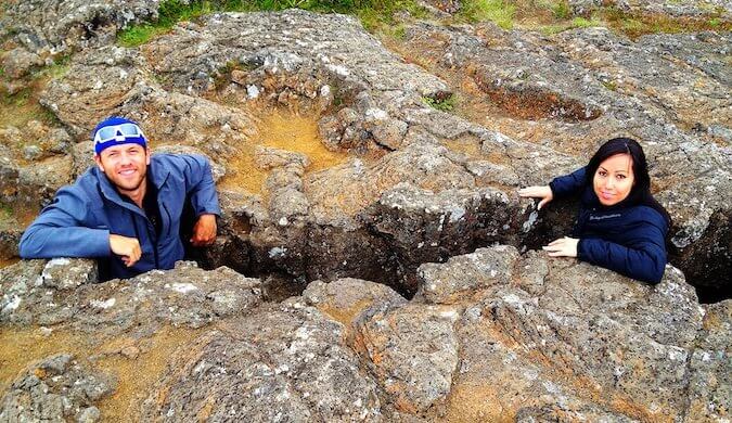 man on left and woman on right both stood in a crevice of a large rock formation