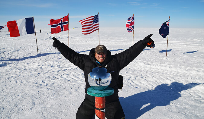 Man celebrating an achievement with arms in the air in a place covered in snow with various countries flags behind him