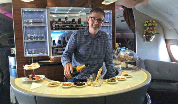 man pouring champain standing behind a bar on an Emirates plane in first class.