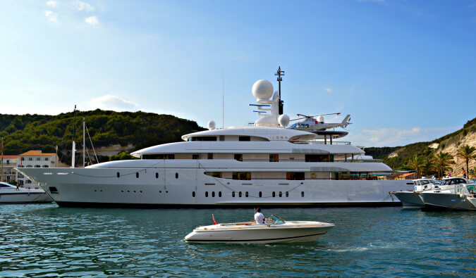 large white yacht with smaller boats next to it in the sea docked