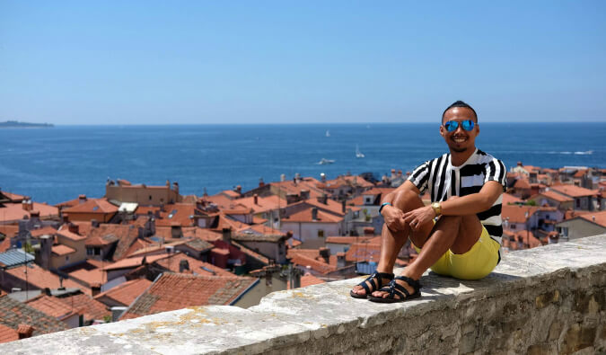 man sitting on a wall in foreground in the background below there are houses and the sea