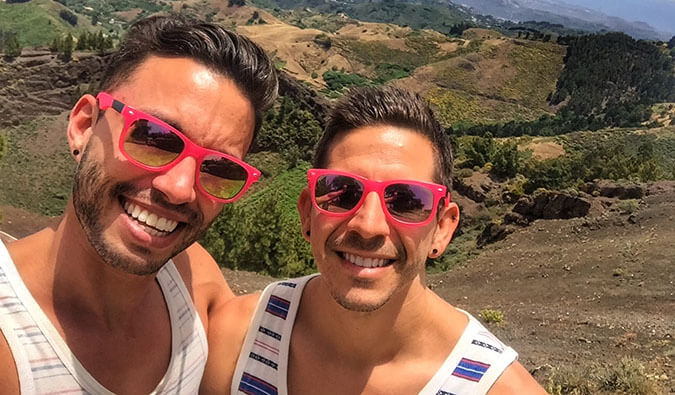 Image of Auston and David smiling wearing matching red sunglasses with a scening background