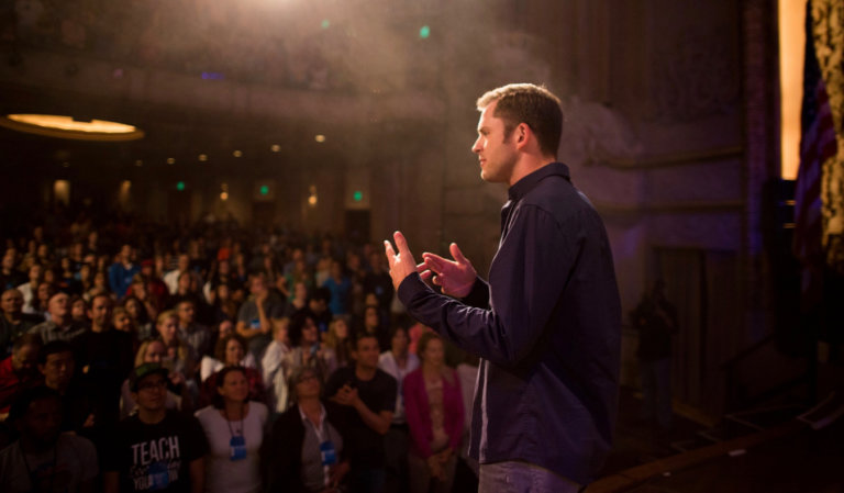 Chris Guillebeau on stage speaking to a large crowd