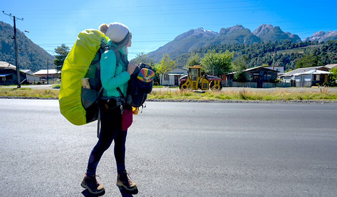 female backpacker walking down a quiet street with mountains in the distance