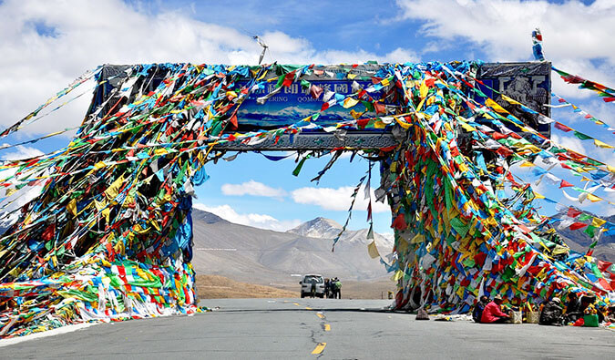 a open road in china with a single car and people. colorful flags decorate a sign over the road