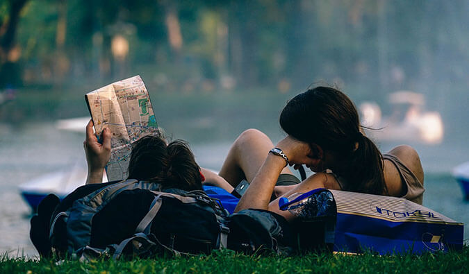 a male and female backpacker relaxing on the grass leaning on their backpacks reading a map