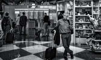 A black and white photo of a solo traveler at the airport looking at his phone