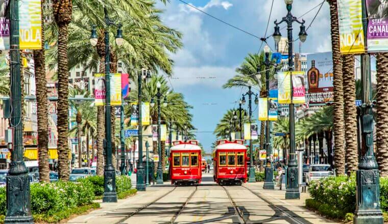 Old trams side by side on a historic tree-lined street in NOLA