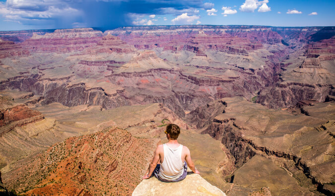 man sat on a rock front and centre in background surrounded by canyon