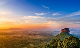 Sunrise over an expansive lush landscape with Sigiriya rock, a large rock formation, rising above the trees in Sri Lanka