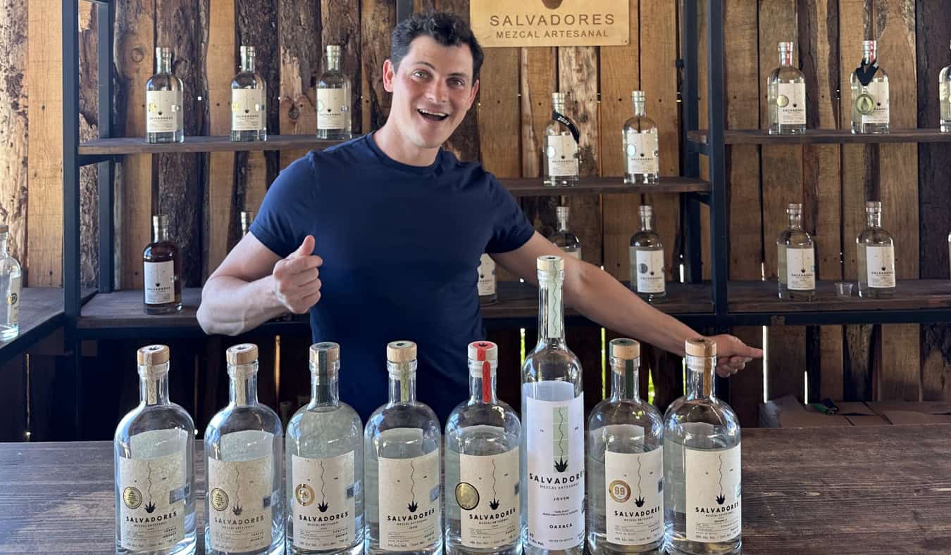Nomadic Matt standing in front of a line of mezcal bottles in Mexico