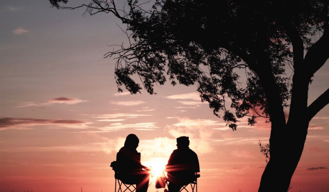 a couple looking at the sunset under a tree