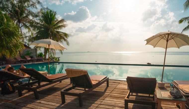 Lounge chairs by the deck of an infinity pool surrounded by palm trees at a luxurious resort