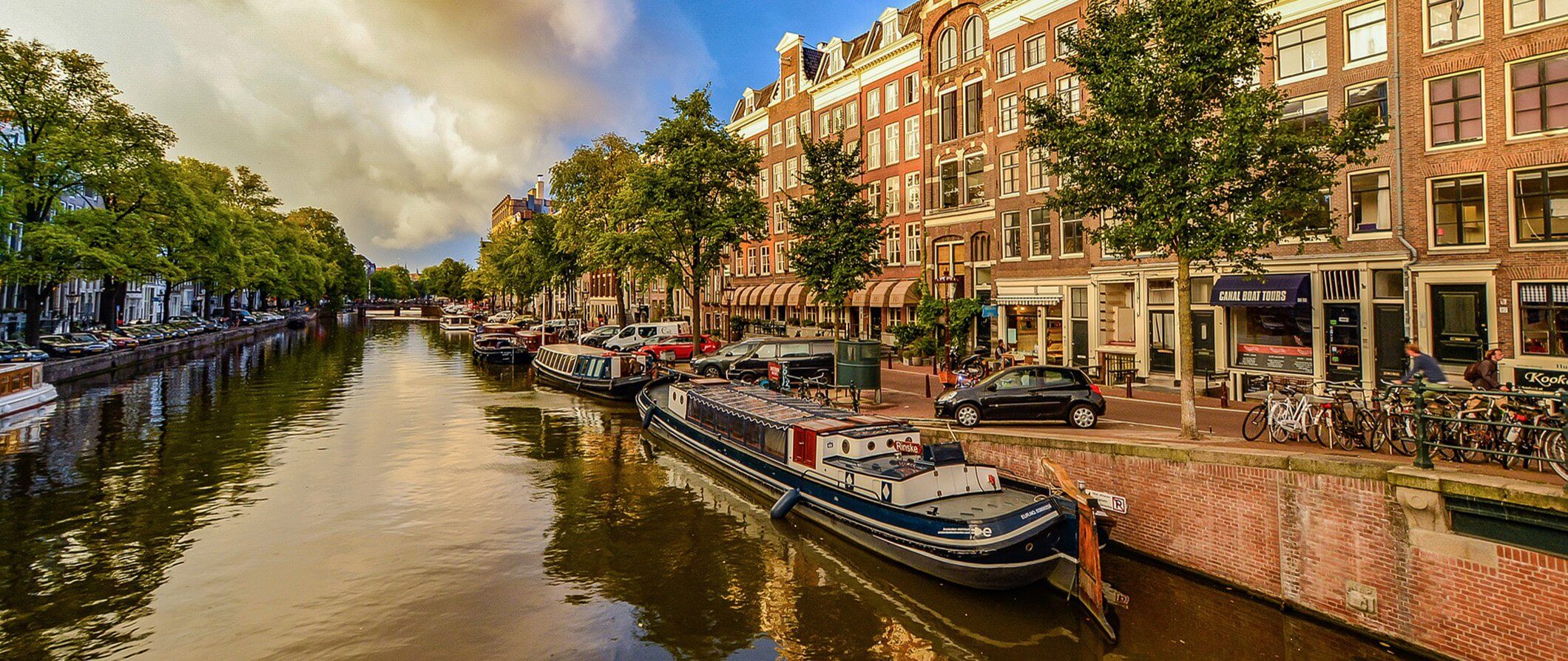 street scene in Amsterdam with the canal running through the middle. Barges moored on both sides