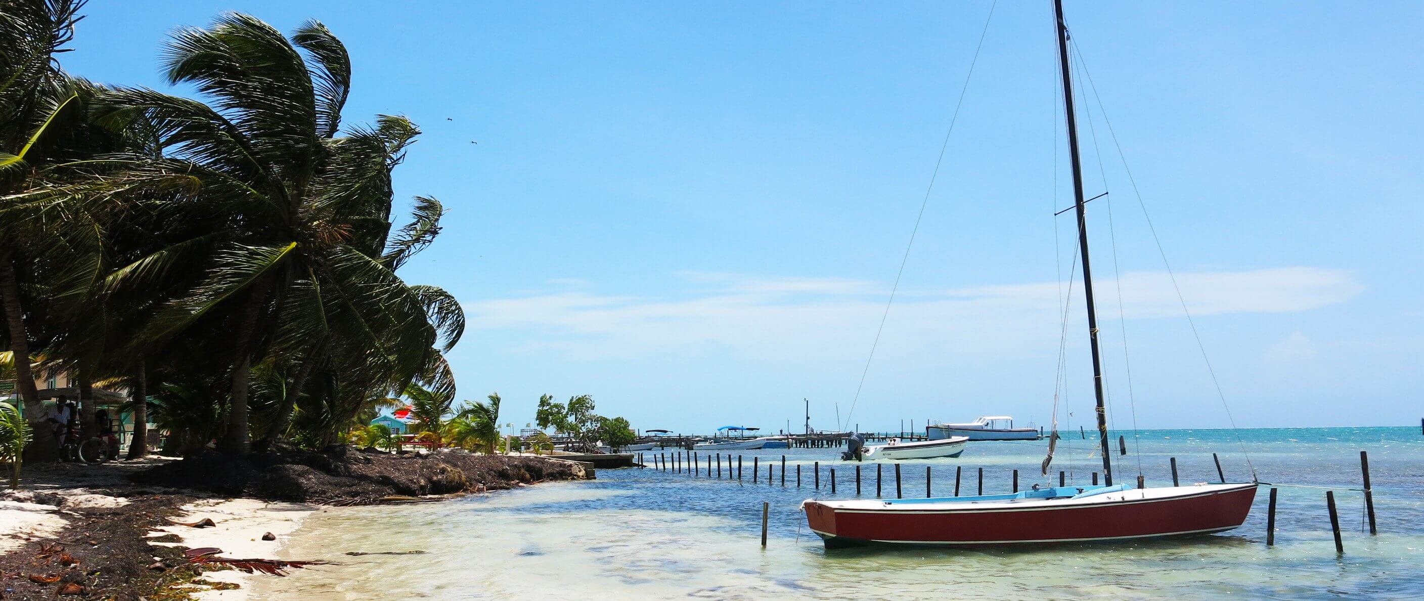 the beach in Caye Caulker, Belize. Sail boat up on the sand. Palm trees