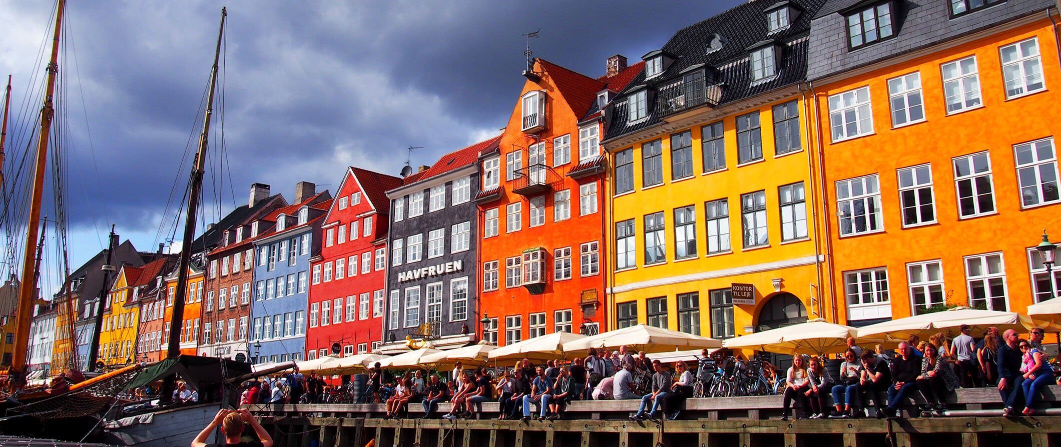 colorful houses in Copenhagen in a street next to a river. People drinking in pubs sitting outside next to the river