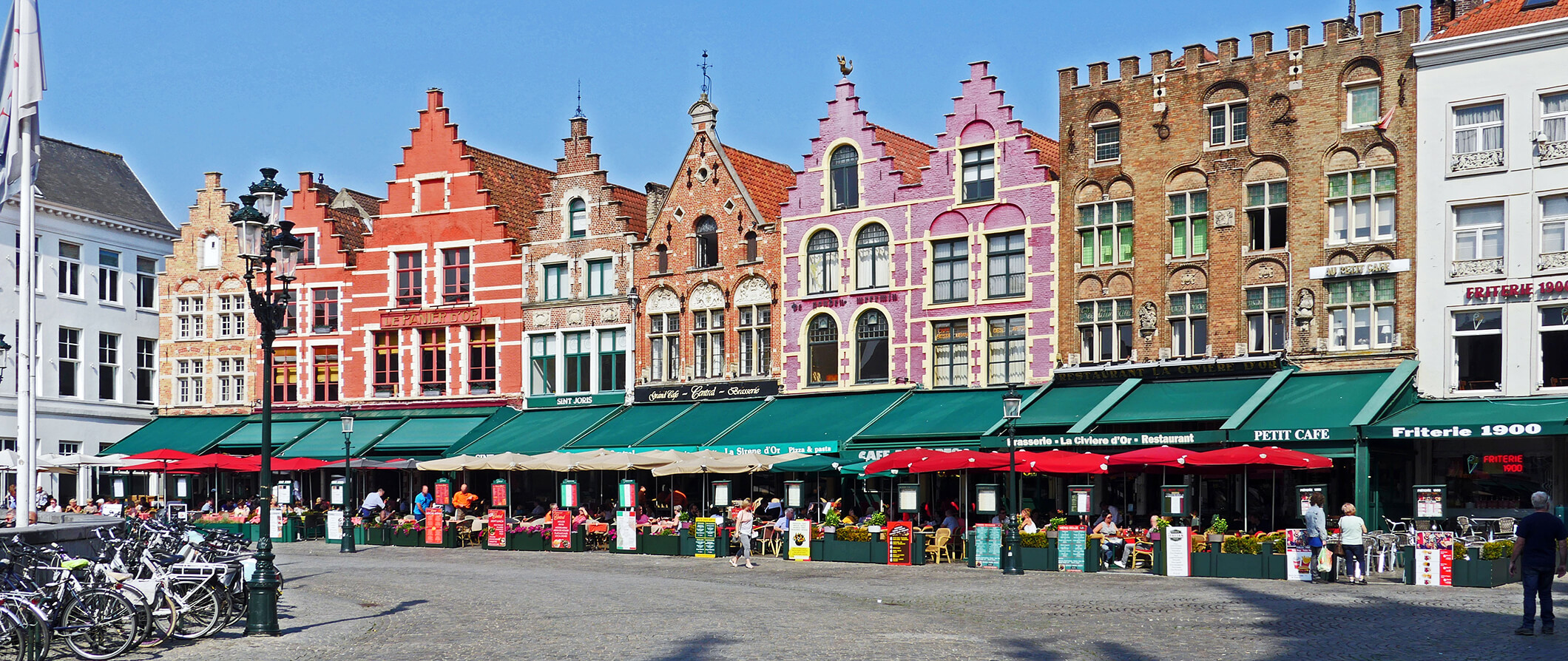 pretty, colorful shops in a row on a street in Belgium. Restaurants with people eating inside and outside.