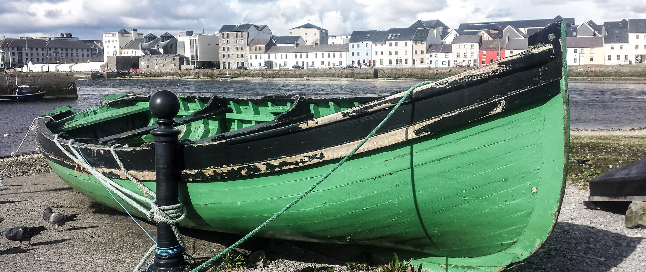 a green boat tied up next to a river in Galway Ireland