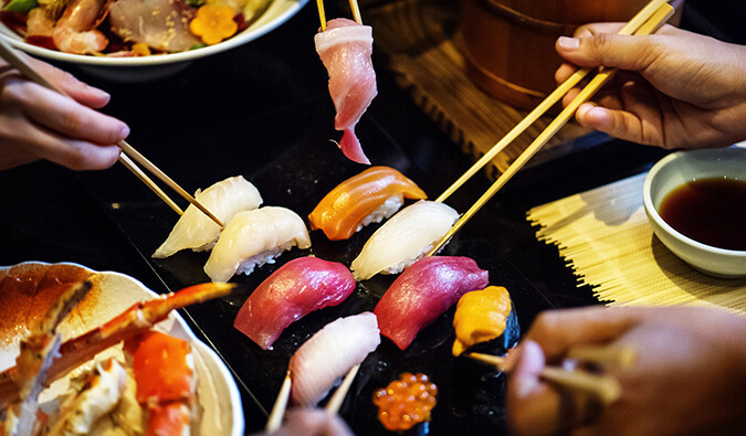people eating Sushi in Tokyo using chopsticks