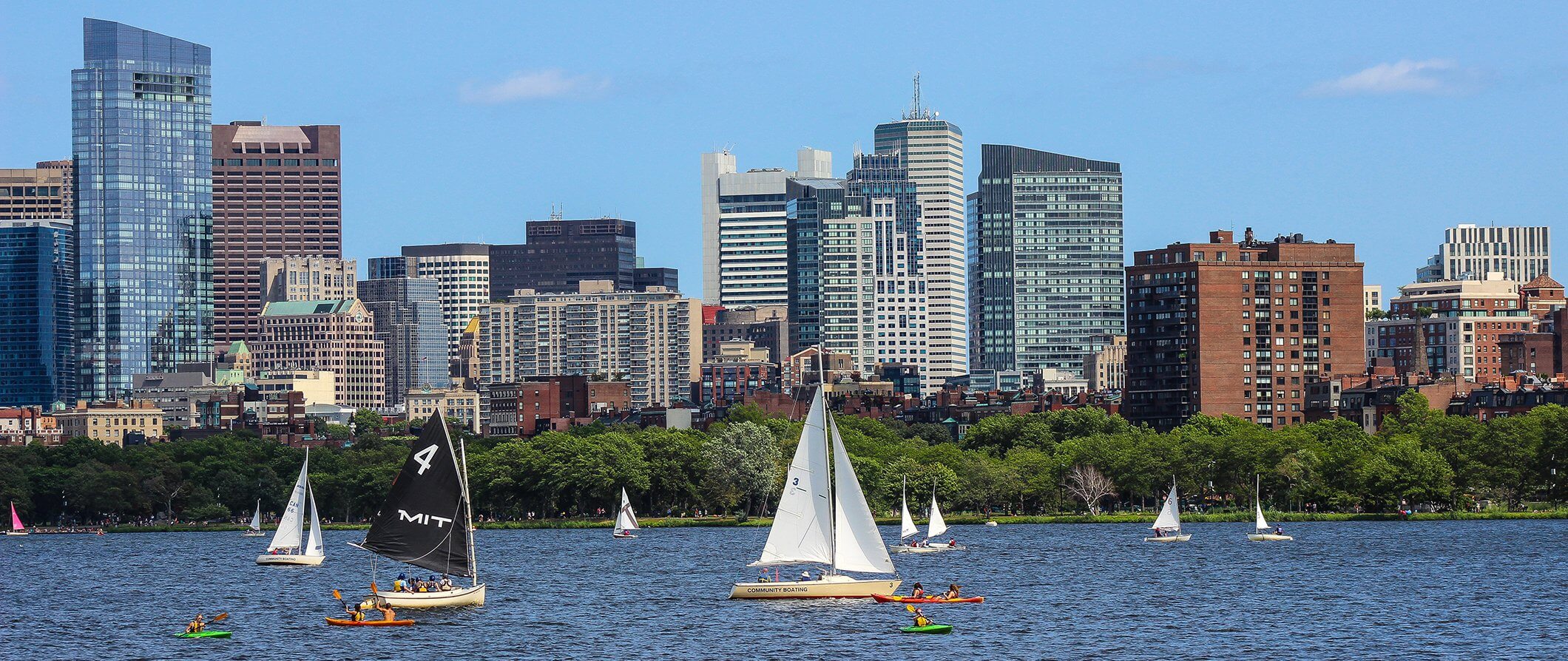 view of Boston taken from the river. Sailboats on the river tall buildings in the background.