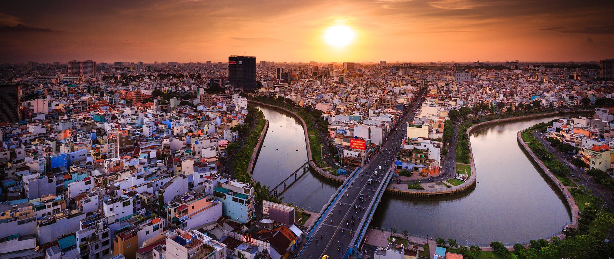 Areal image of Hochi. River, sunset, houses, and cars on a bridge.