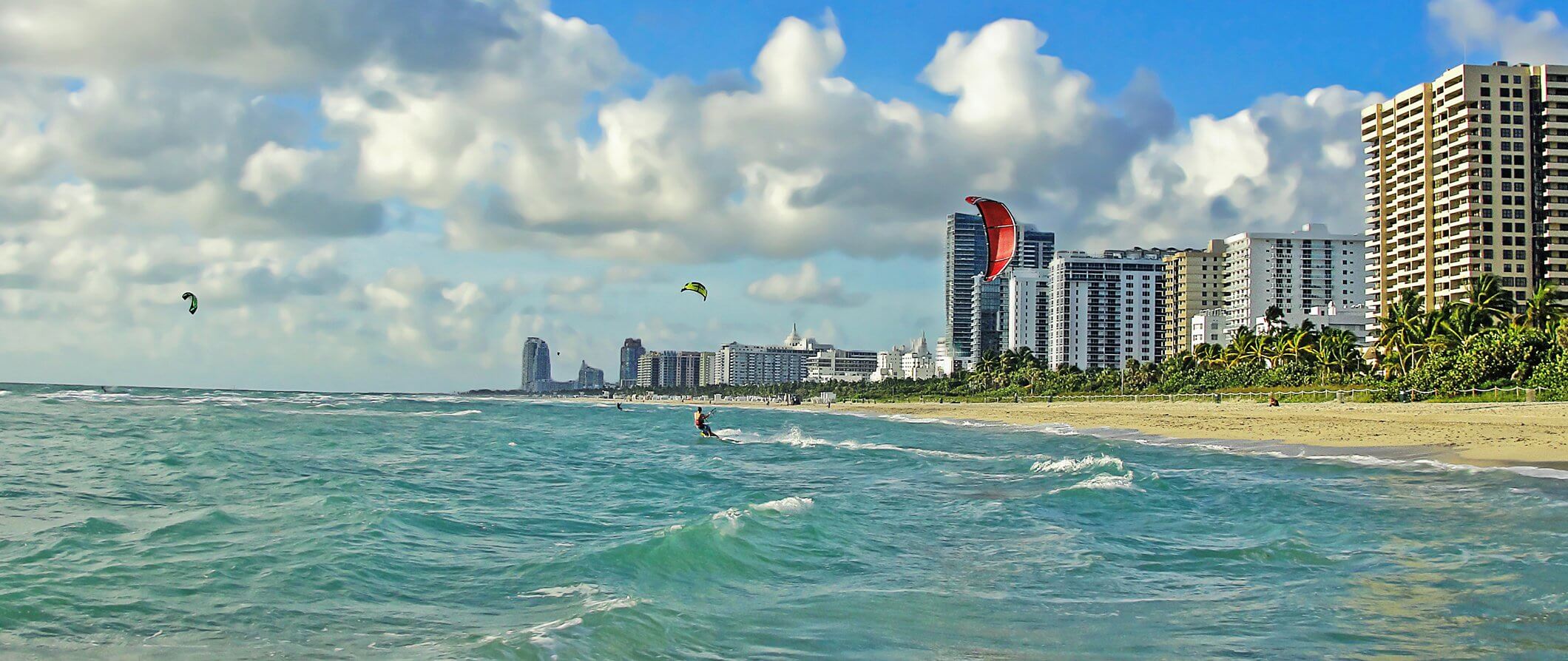 Miami beach with tower blocks to the right. Kite surfers in the sea.