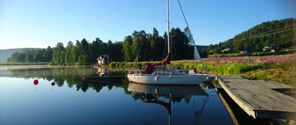scenic image of a lake in Sweden with a sailboat docked and a small house in the background