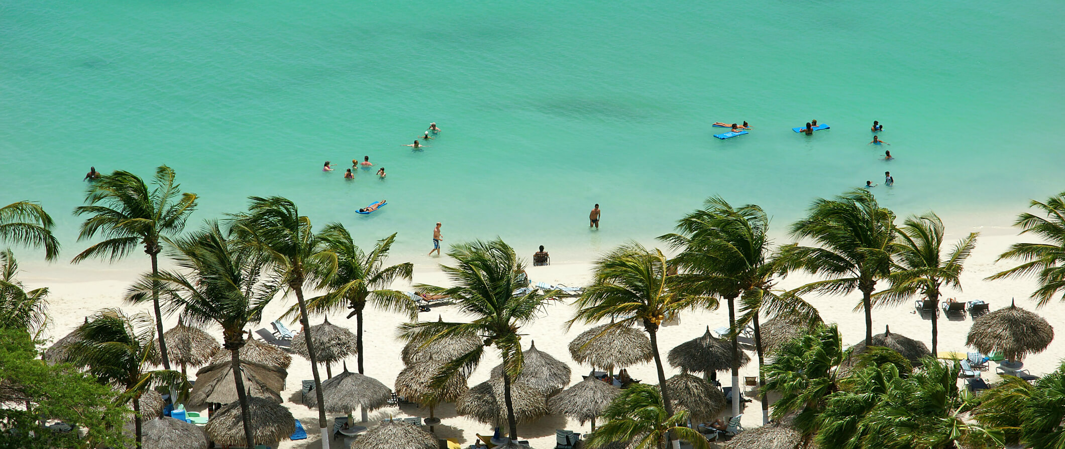 Aruba areal shot looking down on the beach with people sunbathing and swimming in the green sea