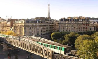 A train crosses a bridge in the foreground with the Eiffel Tower in the background in Paris, France
