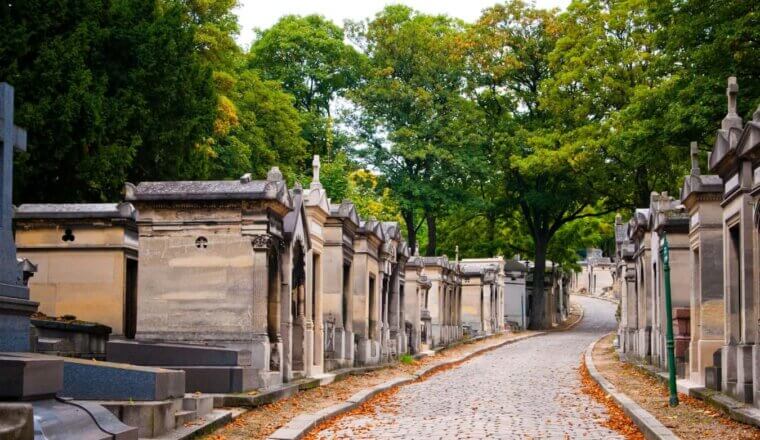 Mausoleums lined up along a cobblestone pathway littered with orange leaves at Pere Lachaise Cemetery in Paris, France