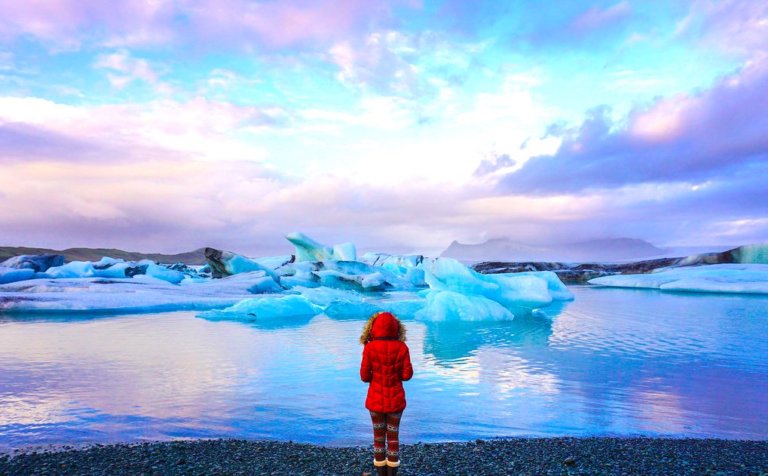 solo female traveler in a read coat at the Glacier Lagoon in Iceland