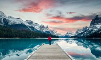A traveler standing on a dock surrounded by nature in the rugged mountains of Canada