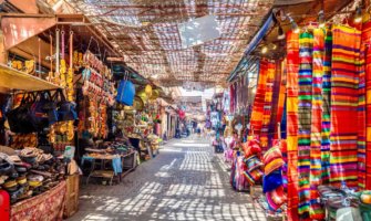 A narrow alleyway in a quiet market in Morocco, lined by small shops selling colorful wares
