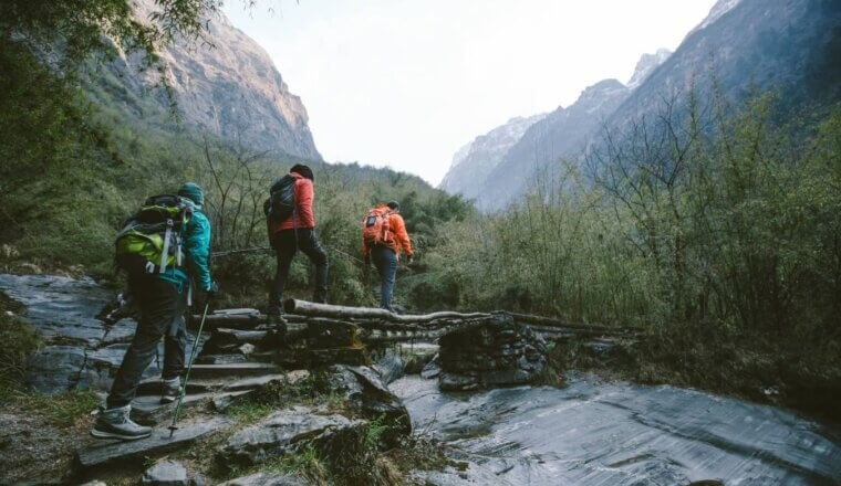 Group of trekkers cross a wooden bridge heading towards mountains in the Annapurna region of the Himalayas