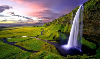 Icelandic waterfall with green landscape and sunset