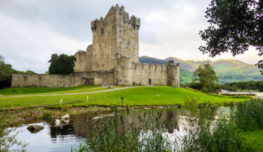 an Irish castle tower on a still lake set against green hills