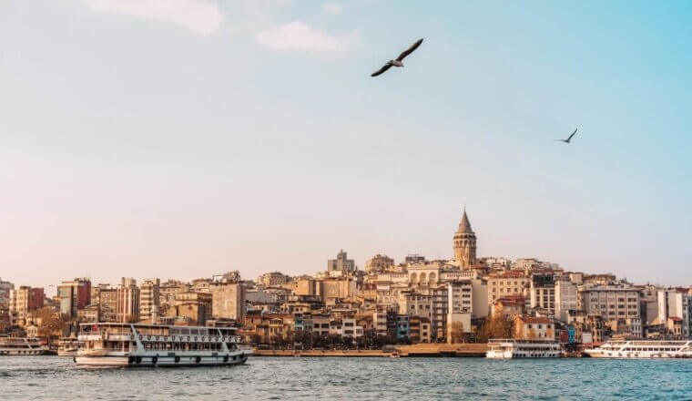 A view of ferries on the Bosphorus River at sunset, with Galata Tower rising above the Istanbul skyline
