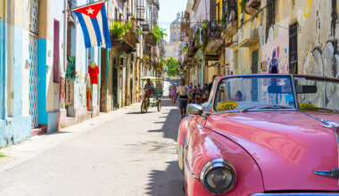 a classic pink car on the colorful streets of Havana, with a Cuban flag in the background