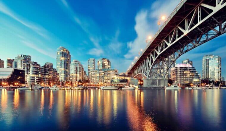The towering Vancouver, Canada city skyline at night lit up and seen from the water near a long bridge